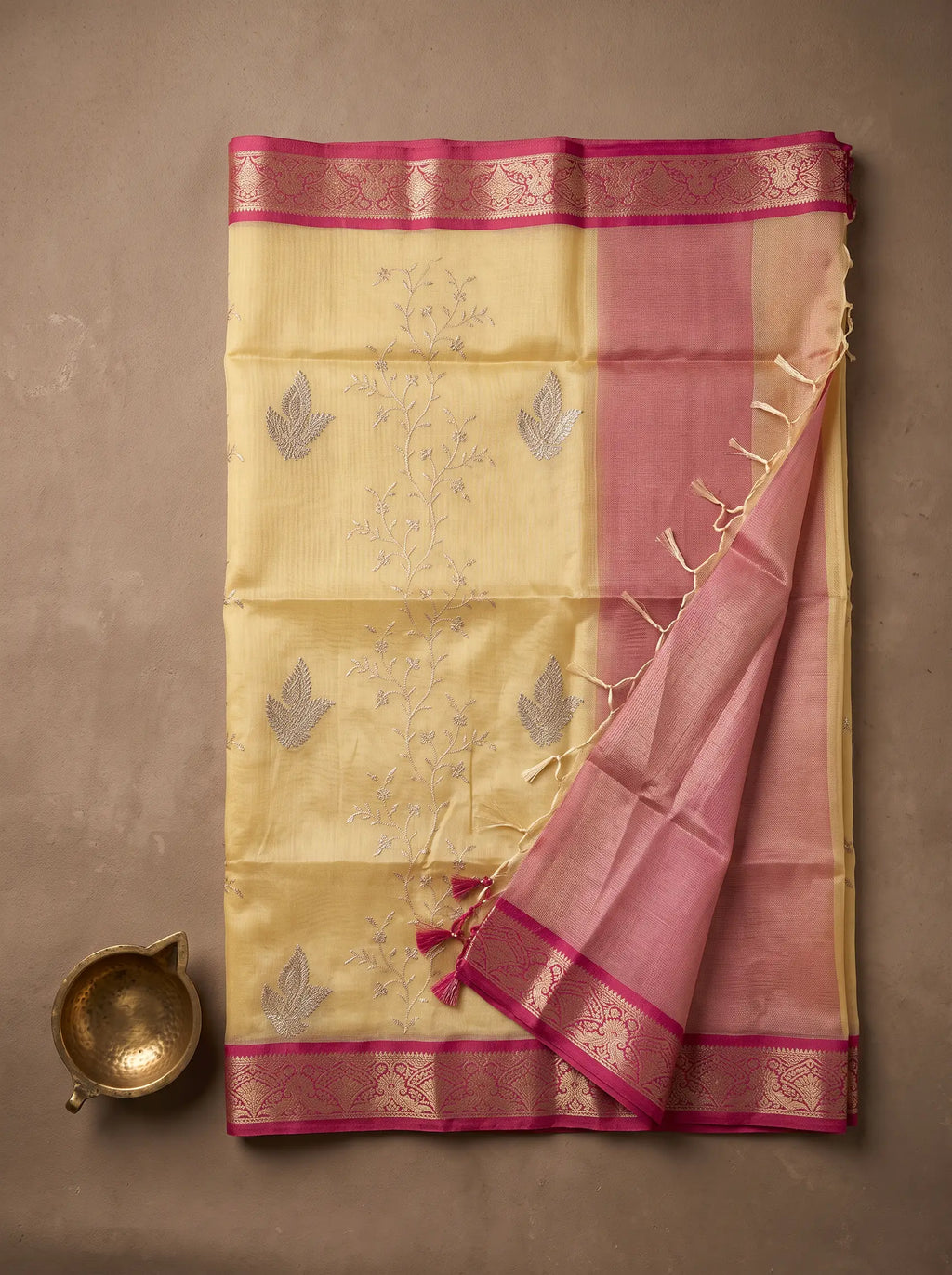 Light gold kota tissue saree displayed flat with pink zari border, embroidered floral motifs and tassled pallu