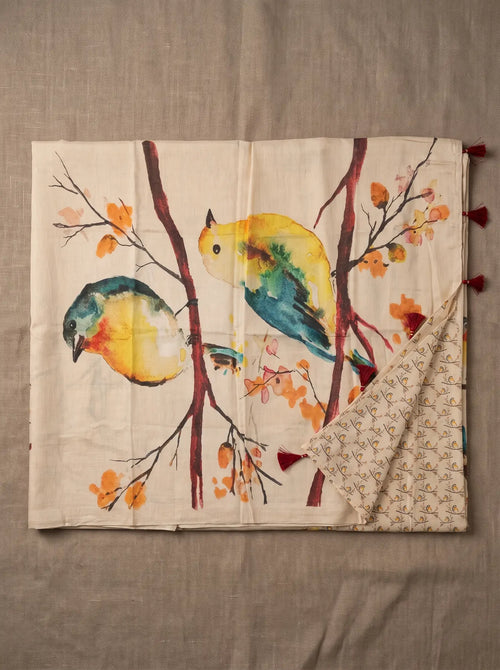 Beige linen saree displayed flat with colourful bird and branch print, printed blouse piece and maroon pallu tassels