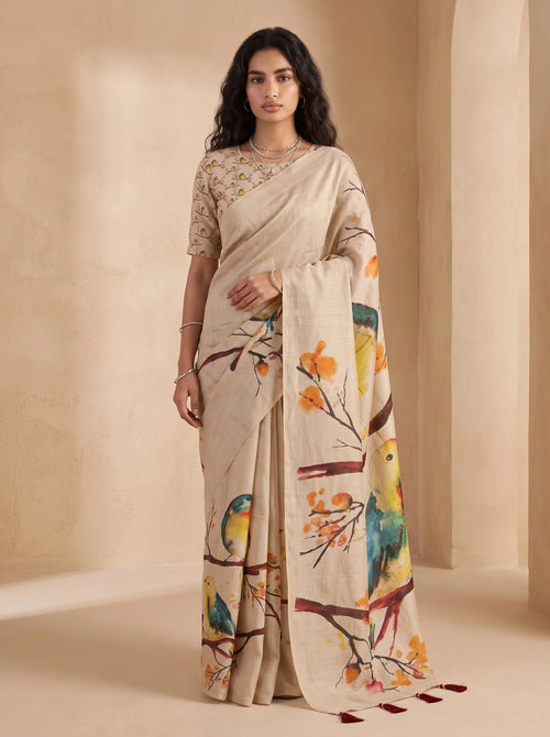 Model wearing beige ready-to-wear linen saree with colourful bird and branch print and tasselled pallu