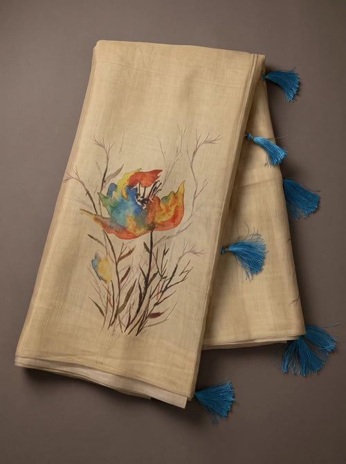 Beige linen saree with colourful floral print and blue tasselled pallu displayed in a flat lay