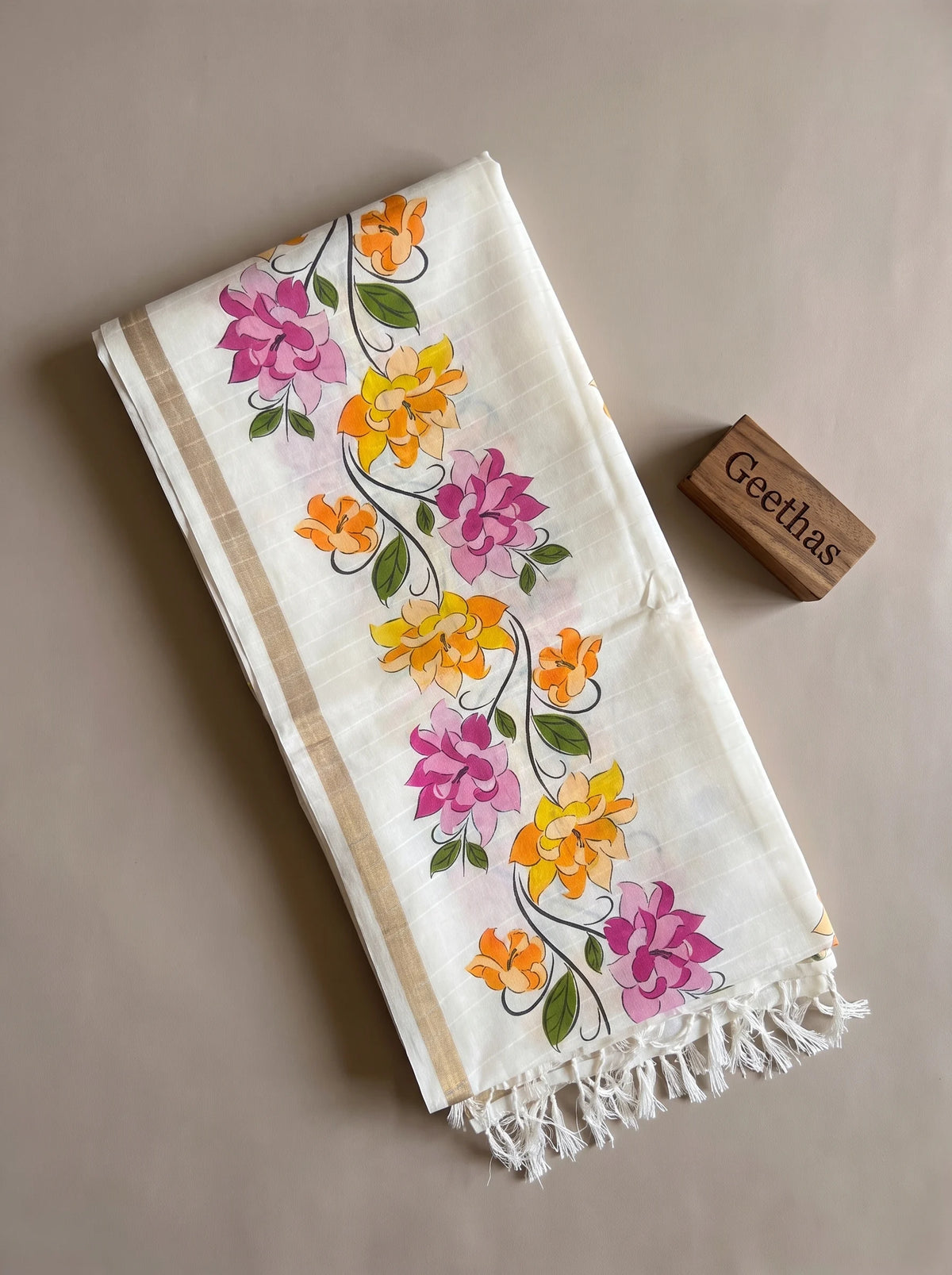 Folded white slub linen saree showing pink and yellow floral print, subtle beige-gold toned border and tasselled pallu