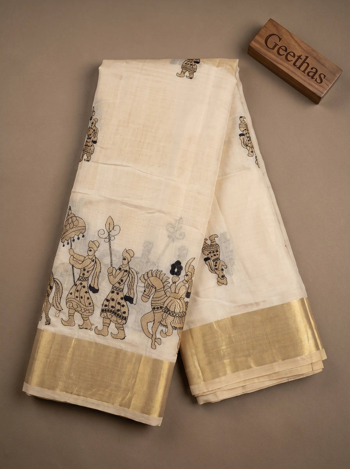 Off-white semi tussar silk saree displayed flat with Rajasthani folk motif embroidery and gold-toned border