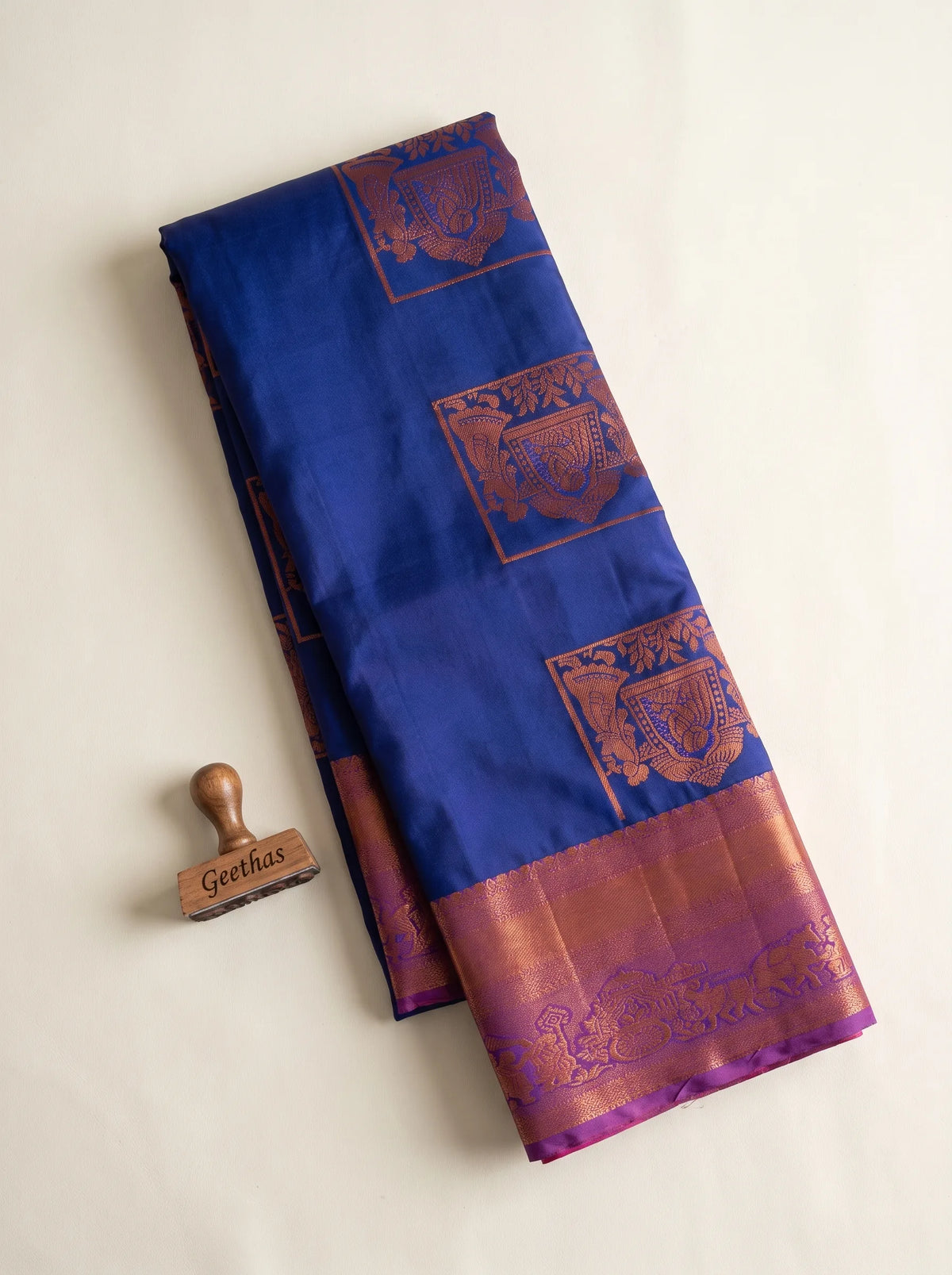 Folded royal blue semi silk saree with copper-toned woven motifs and magenta decorative border