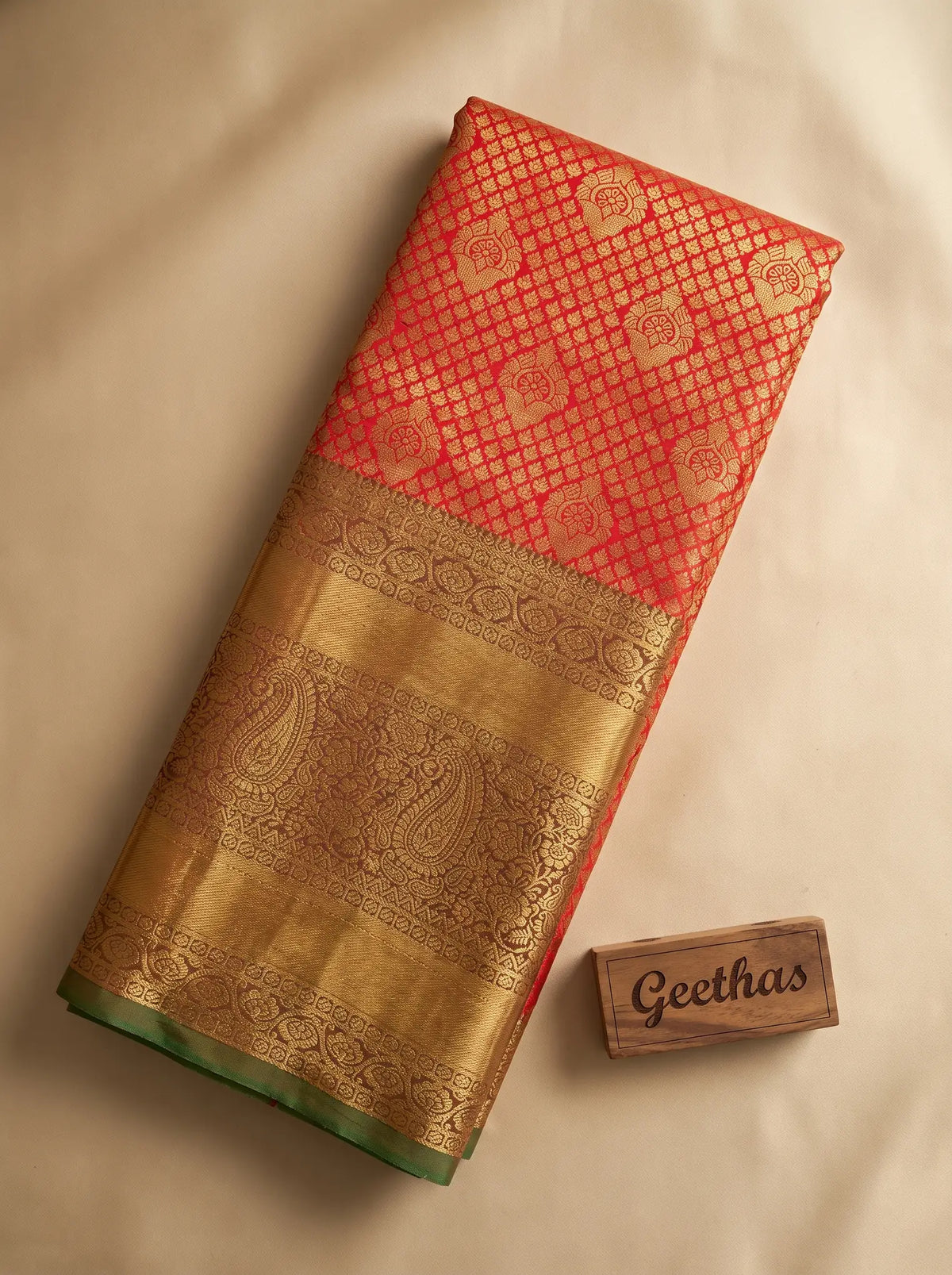 Vermilion orange semi silk saree folded to display its gold-toned woven paisley border and green edging
