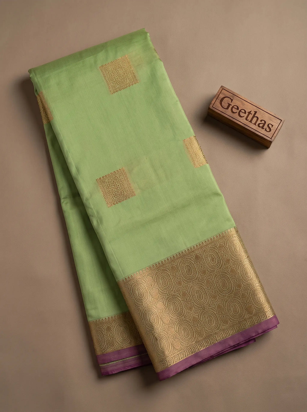 Folded pista green semi silk saree showing gold-toned square motifs and ornate paisley woven border