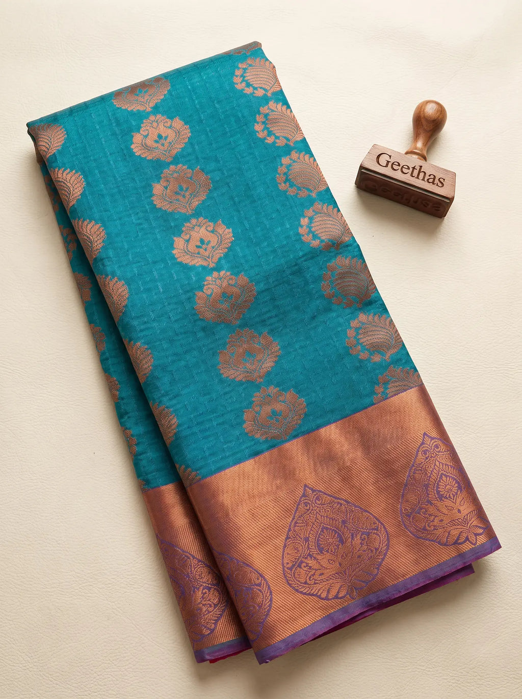 Folded teal blue semi silk saree with copper-toned woven paisley motifs and a broad contrast border