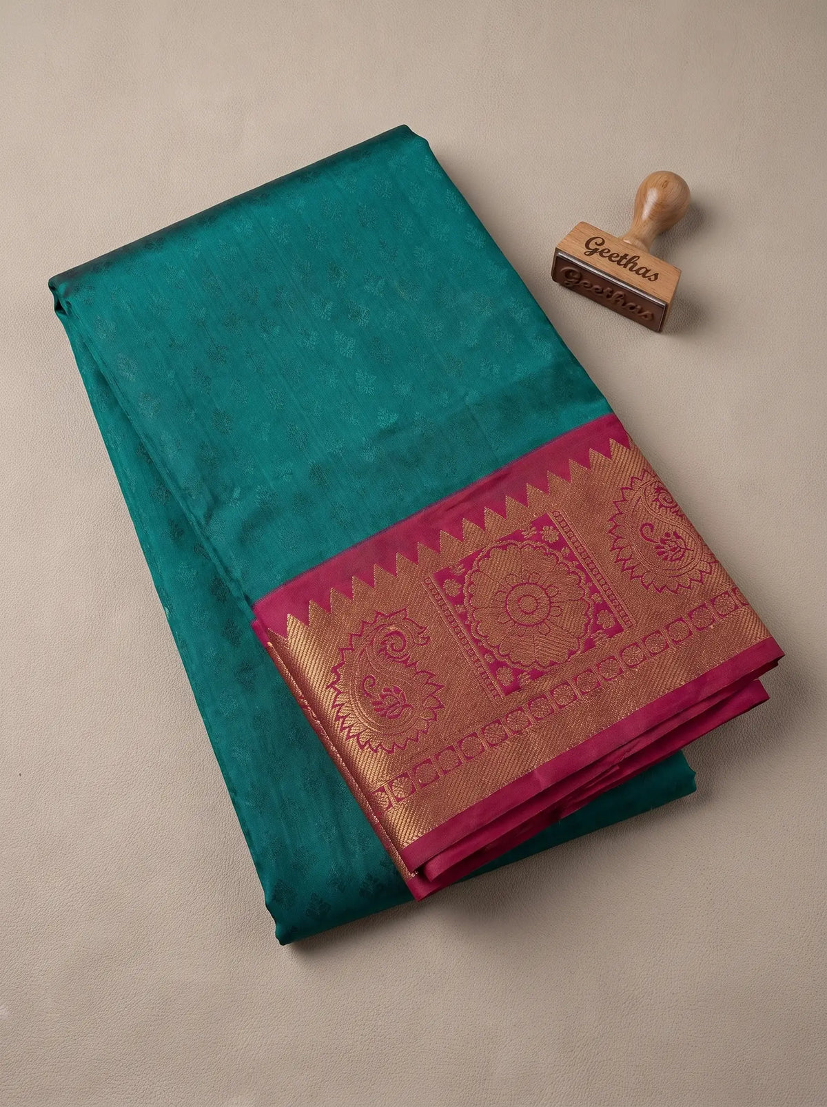 Folded teal blue semi silk saree with a magenta and gold-toned zari woven border
