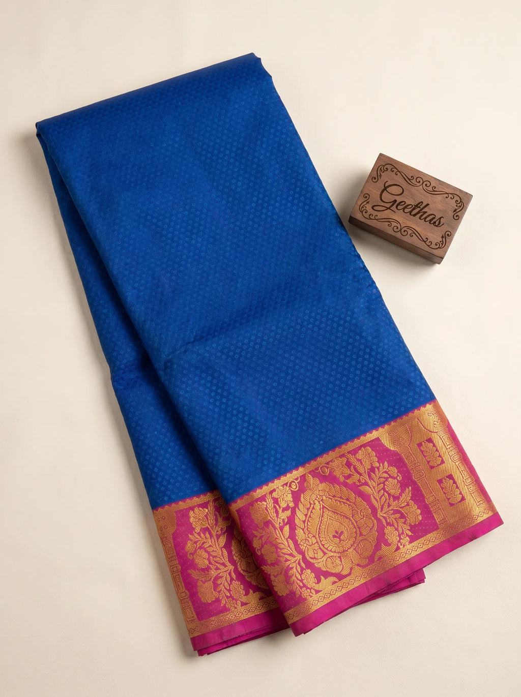 Royal blue semi silk saree with a pink floral gold-toned woven border, displayed folded