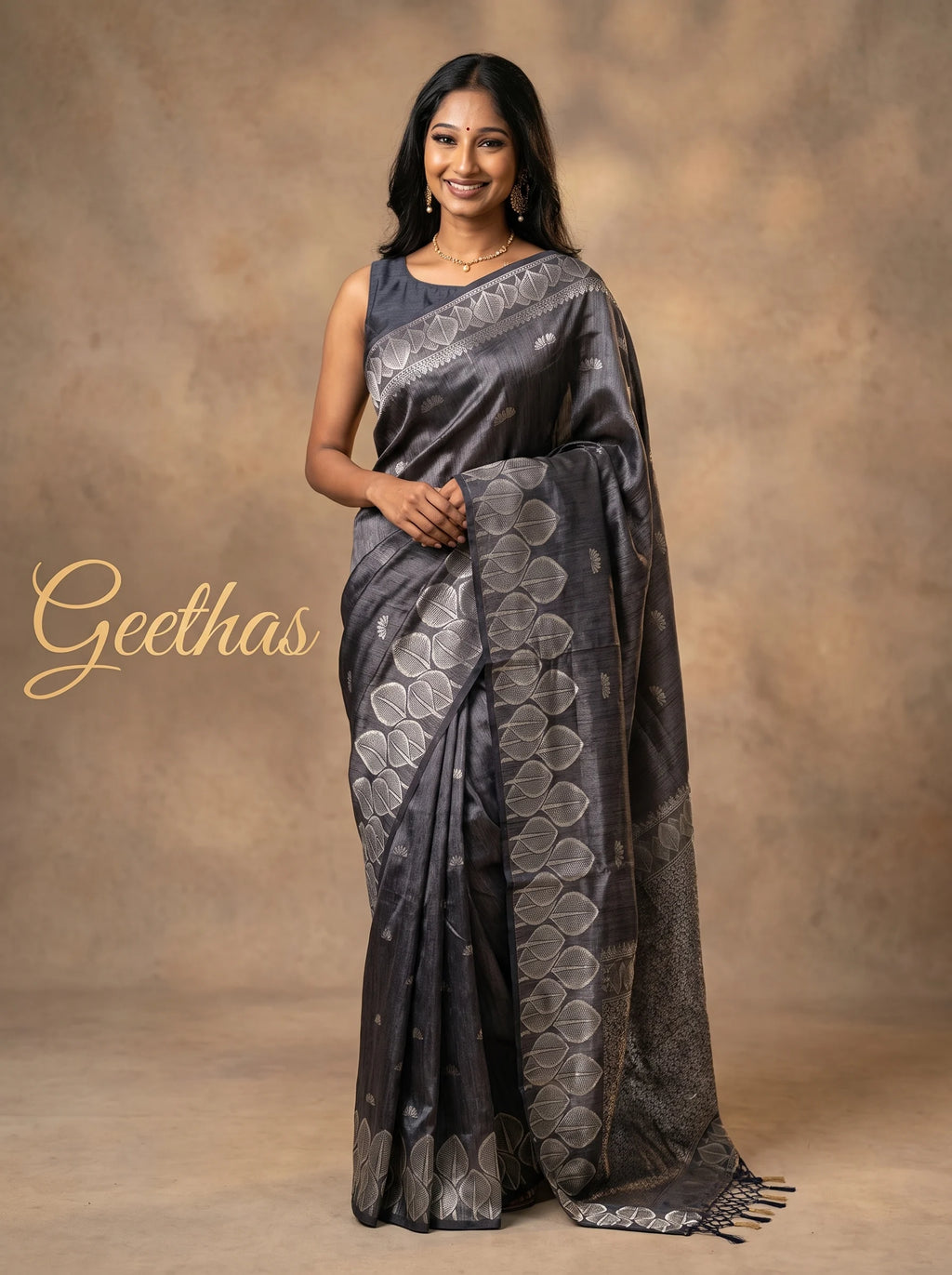Model wearing a charcoal grey soft tissue saree with silver-toned leaf border and tassled pallu