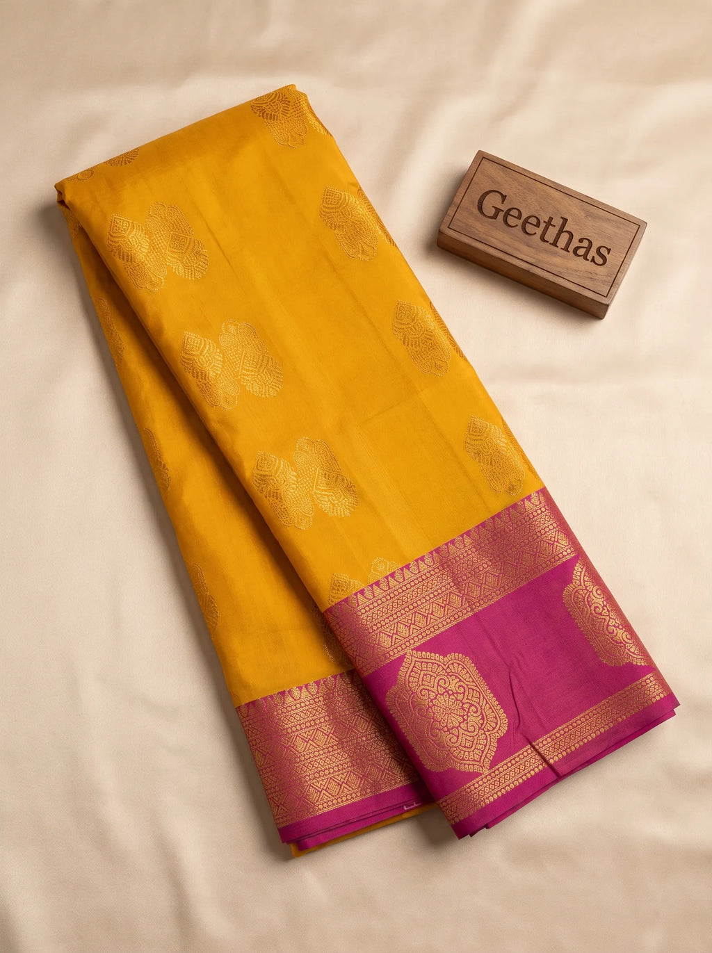 Mustard yellow soft silk saree with gold-toned woven motifs and magenta geometric border displayed flat