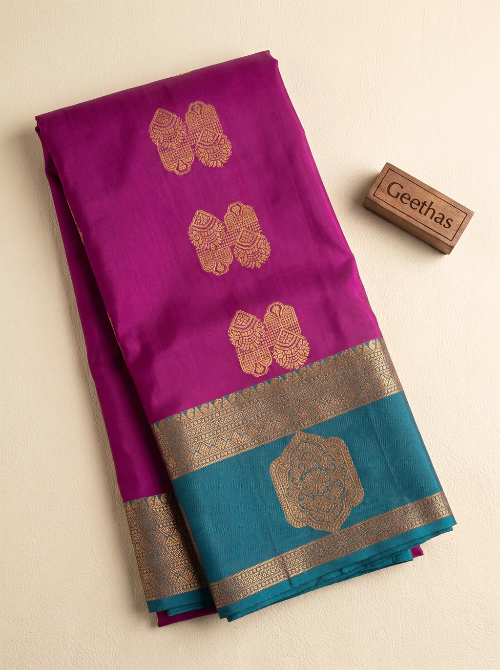 Folded magenta pink soft silk saree with gold-toned woven motifs and contrasting teal decorative border