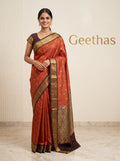 Model wearing rust orange soft silk saree with gold-toned motifs and contrasting deep brown zari border