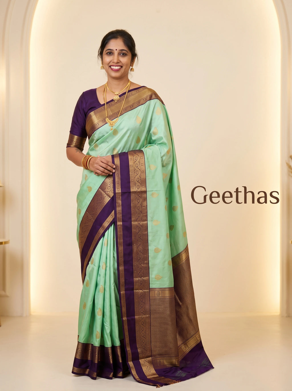 Model wearing a mint green soft silk saree with gold-toned woven motifs and a deep purple decorative border.