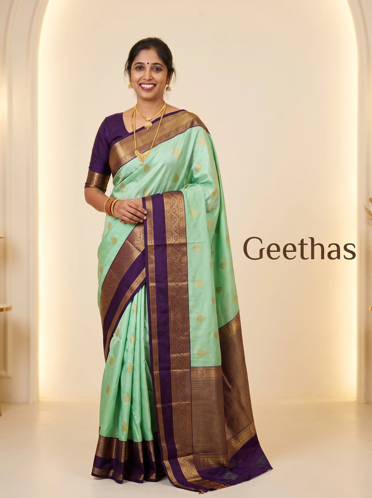 Model wearing a mint green soft silk saree with gold-toned woven motifs and a deep purple decorative border.