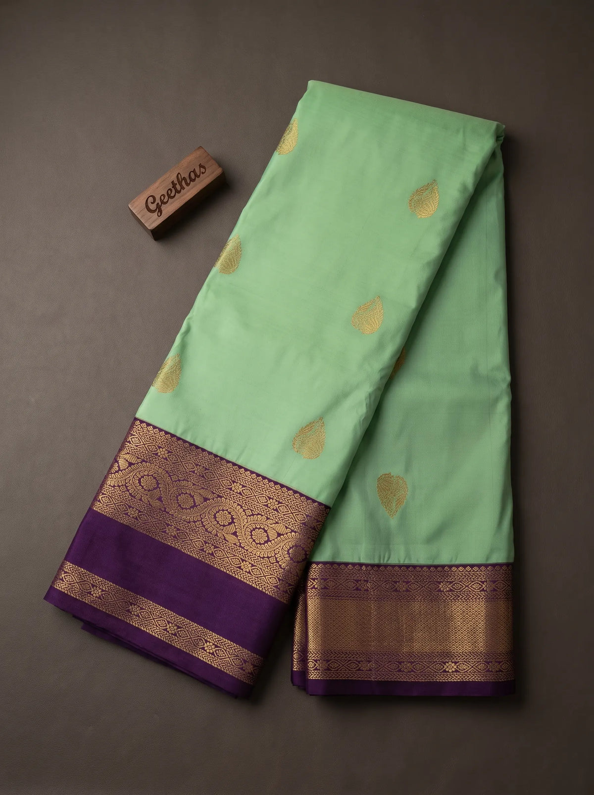 Mint green soft silk saree displayed with gold-toned woven leaf motifs and a deep purple patterned border.