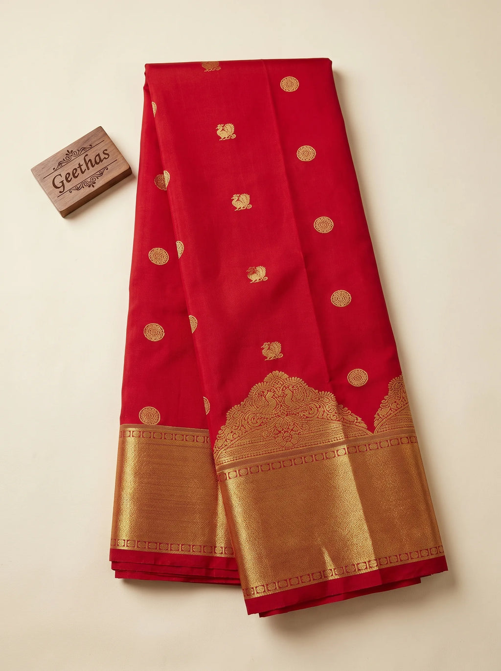 Deep red soft silk saree displayed flat with gold-toned woven motifs and a broad zari border