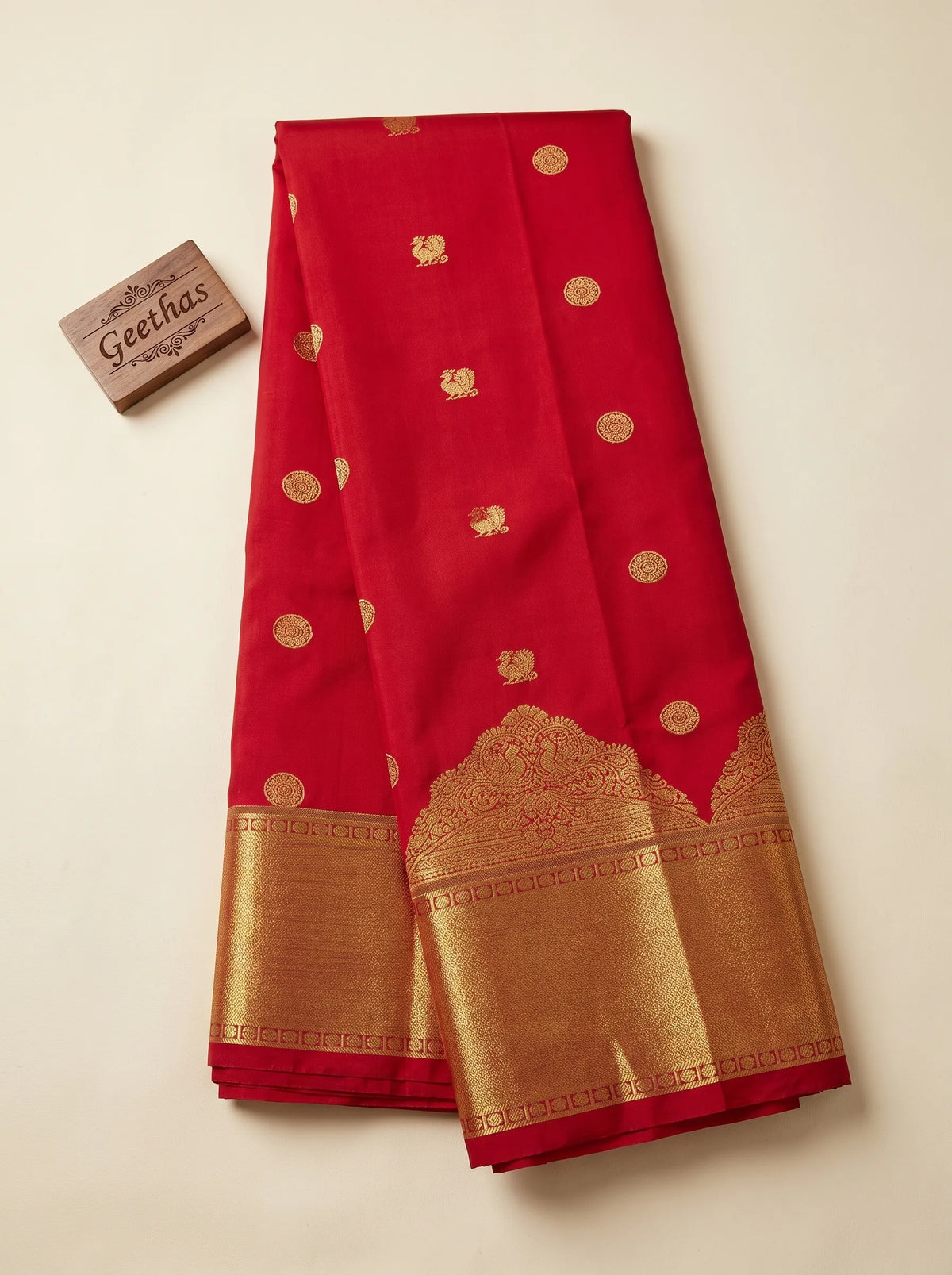 Deep red soft silk saree displayed flat with gold-toned woven motifs and a broad zari border