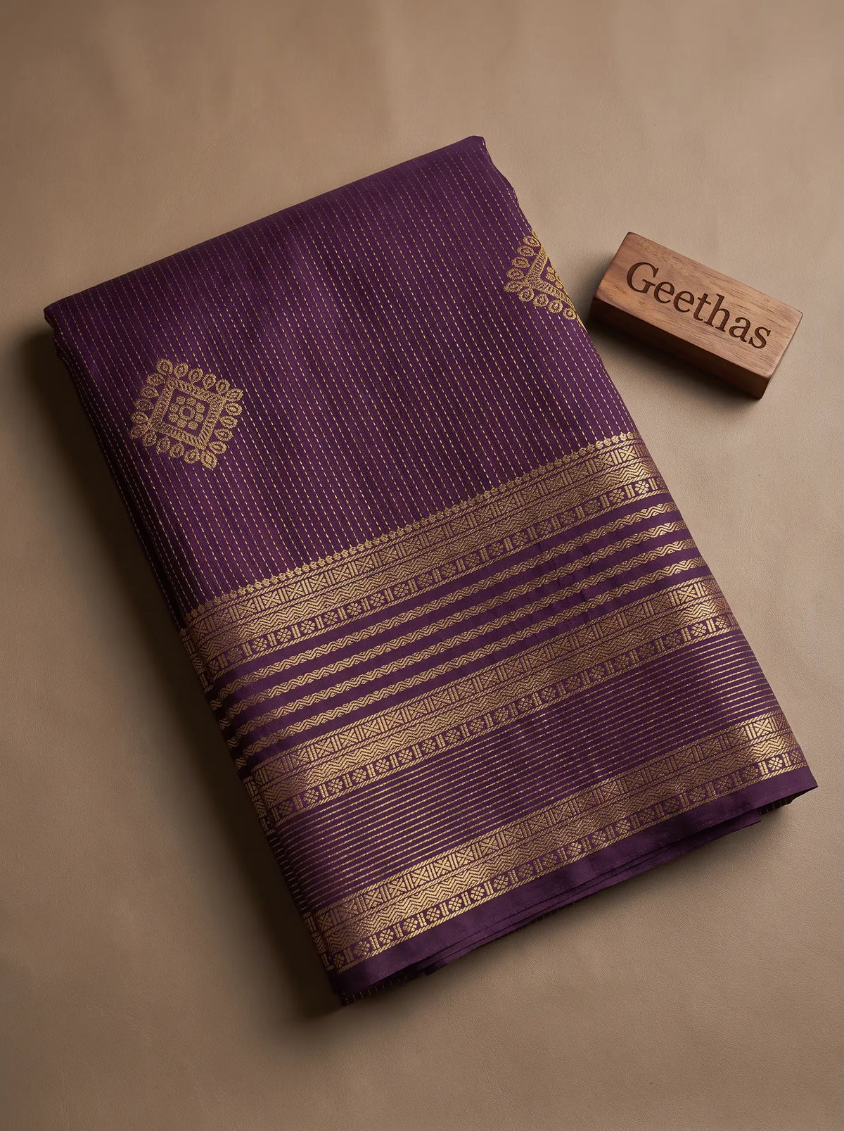Folded dark purple soft silk saree with gold-toned woven geometric border and motifs