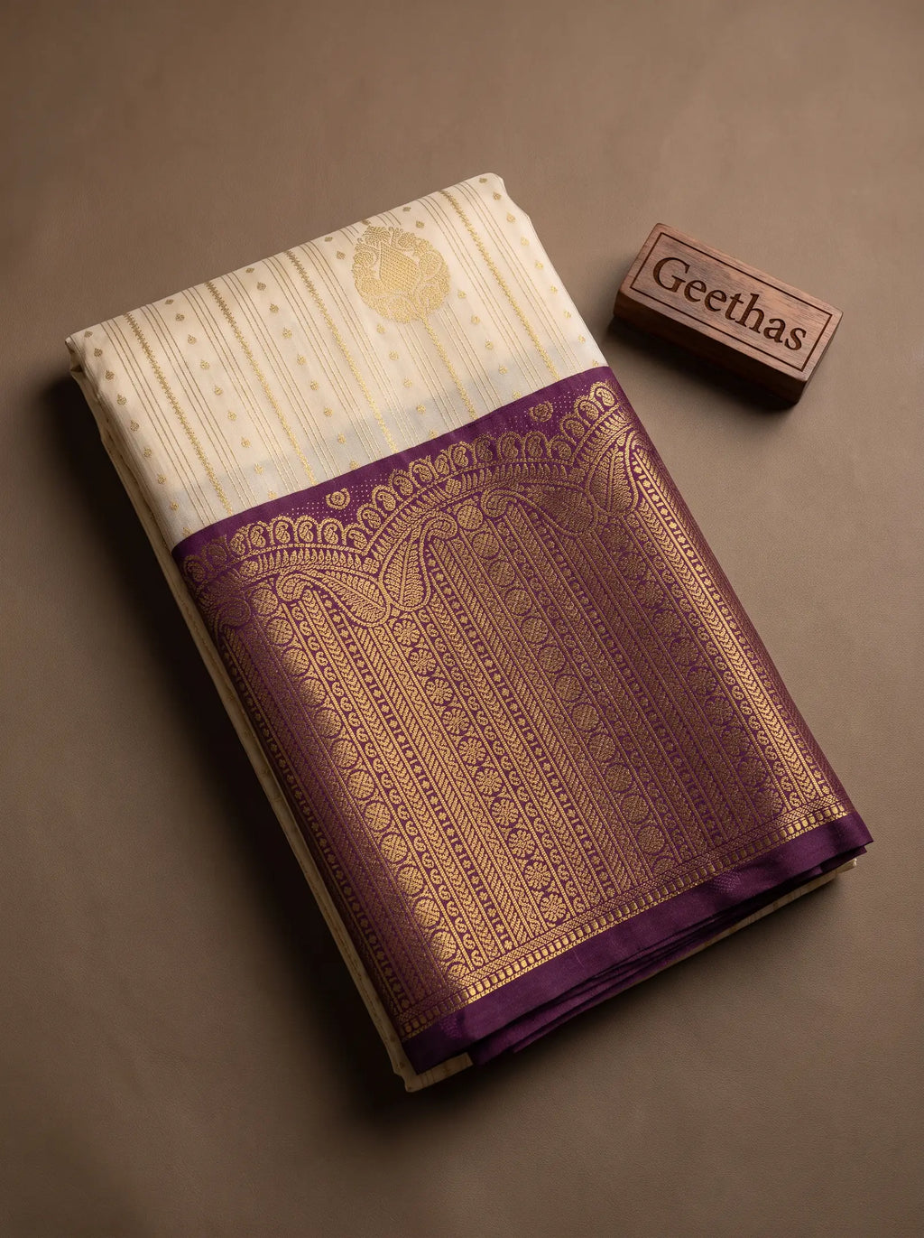 Folded cream soft silk saree with a purple and gold-toned woven border