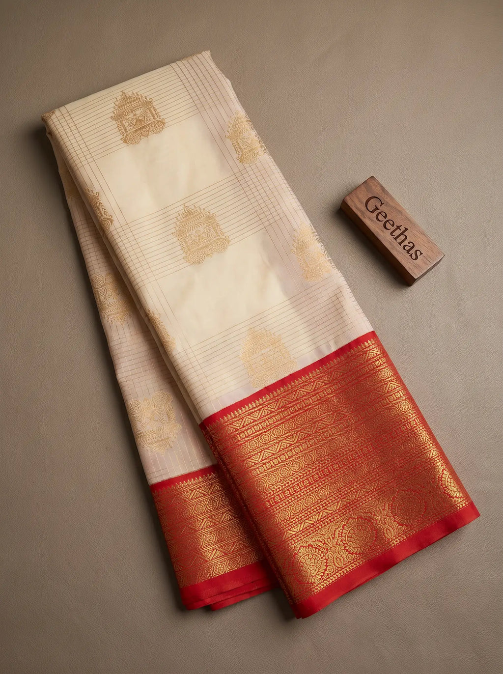 Cream soft silk saree displayed flat with gold-toned woven motifs and a rich red decorative border