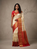 Model wearing a cream soft silk saree with gold-toned woven motifs, red border and red pallu