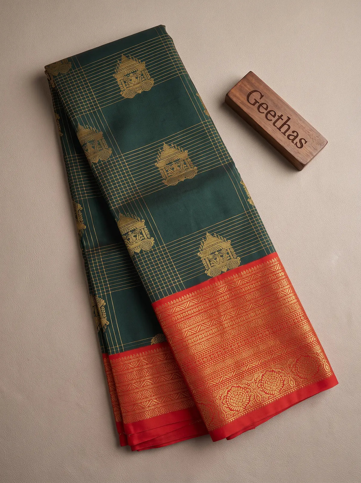 Folded forest green soft silk saree with gold-toned woven motifs and red decorative border