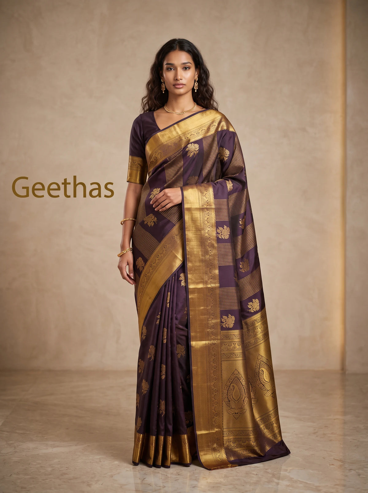 Model wearing a deep brown soft silk saree with gold-toned floral motifs and a broad decorative woven border