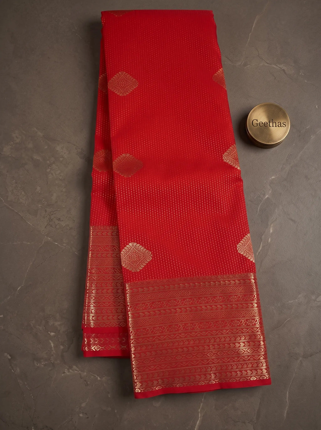 Red soft silk saree displayed flat with gold-toned geometric motifs and a wide woven zari border