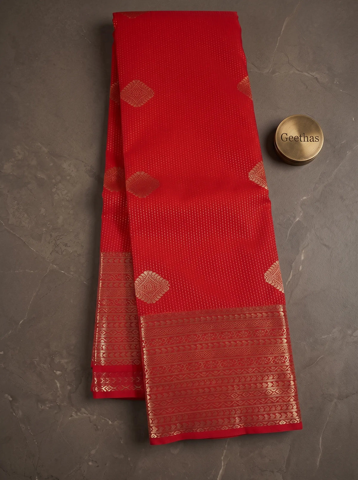 Red soft silk saree displayed flat with gold-toned geometric motifs and a wide woven zari border