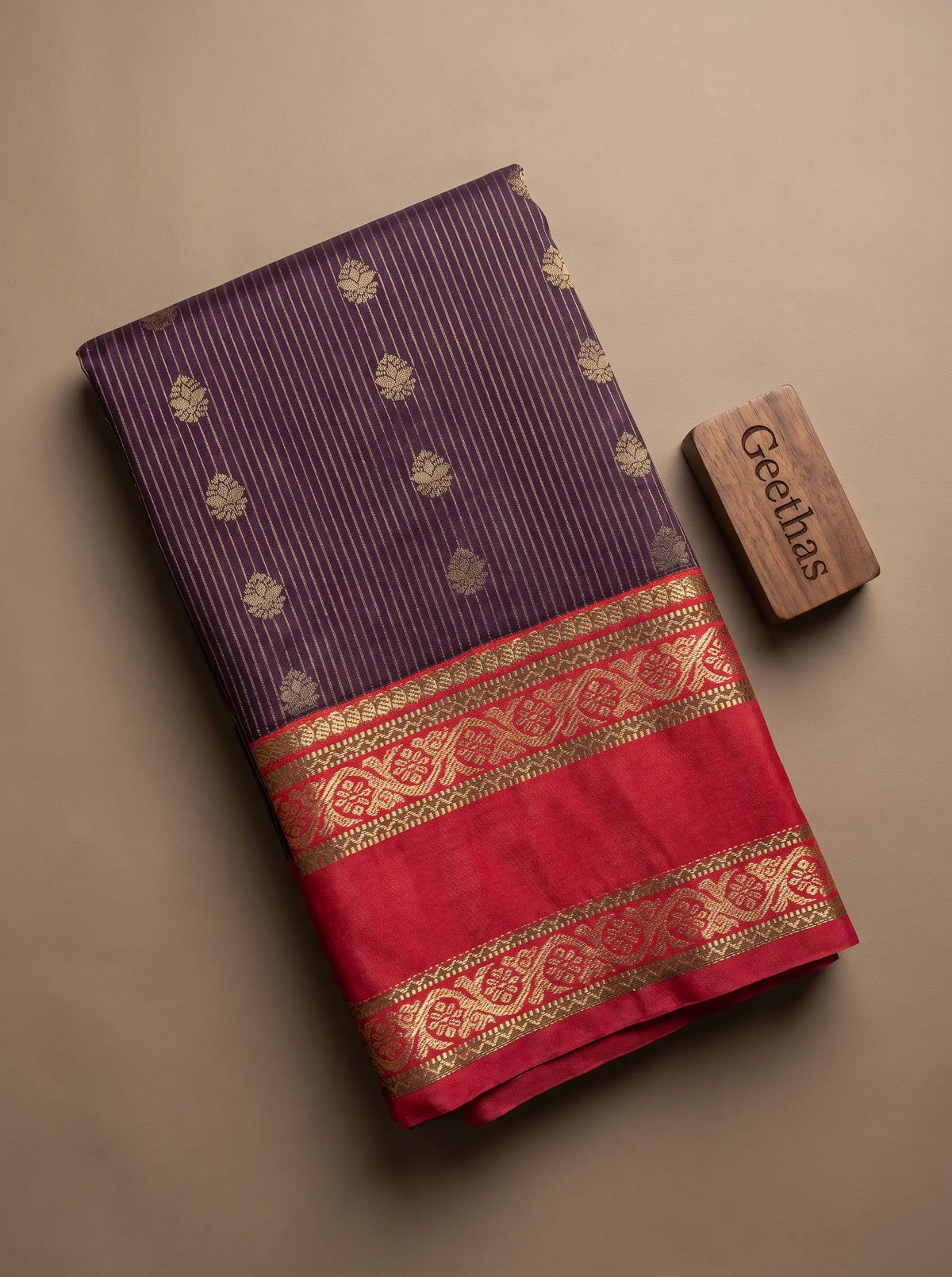 Folded deep purple and rose-pink soft silk saree showing fine striped floral motifs and a decorative gold-toned woven border.