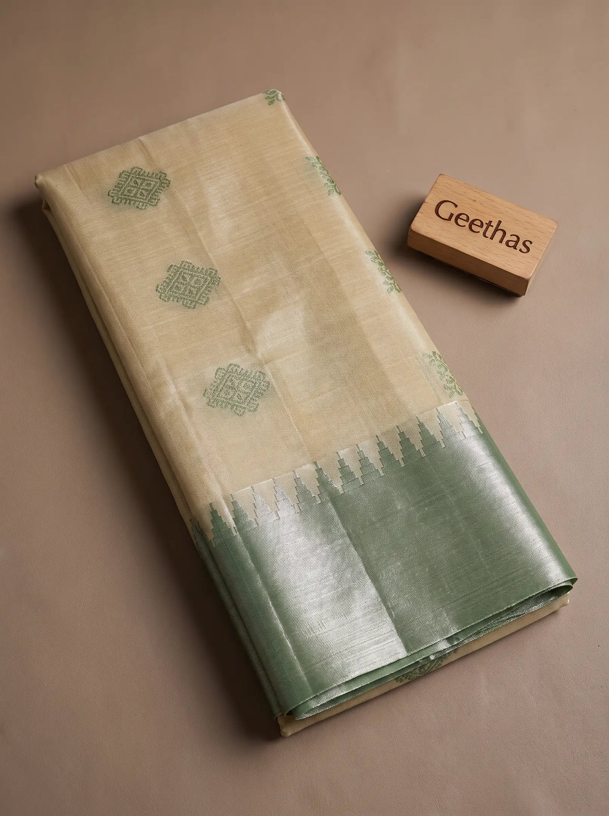 Folded beige tissue soft silk saree with green woven geometric motifs and contrasting green border