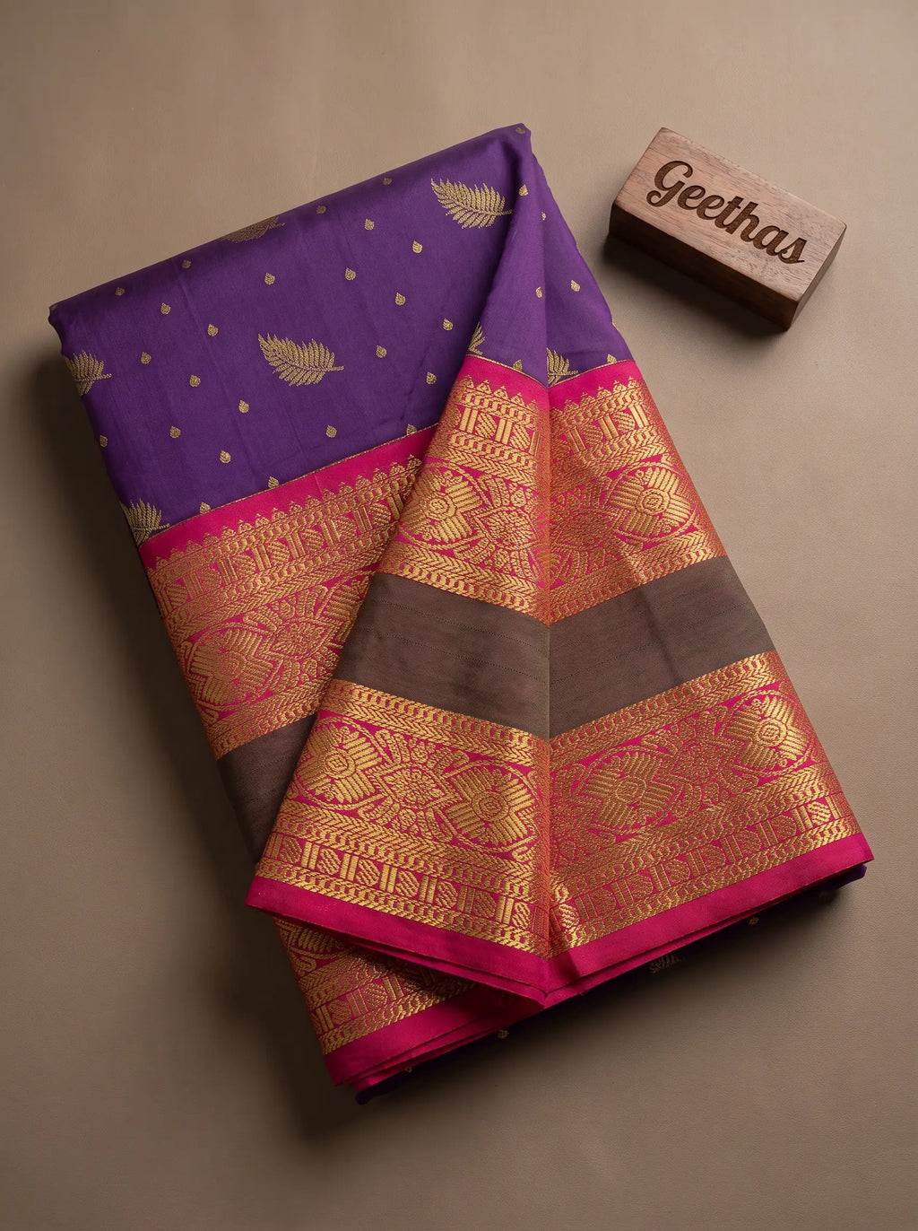 Violet soft silk saree with gold-toned woven leaf motifs and magenta decorative border, displayed in a flat lay.