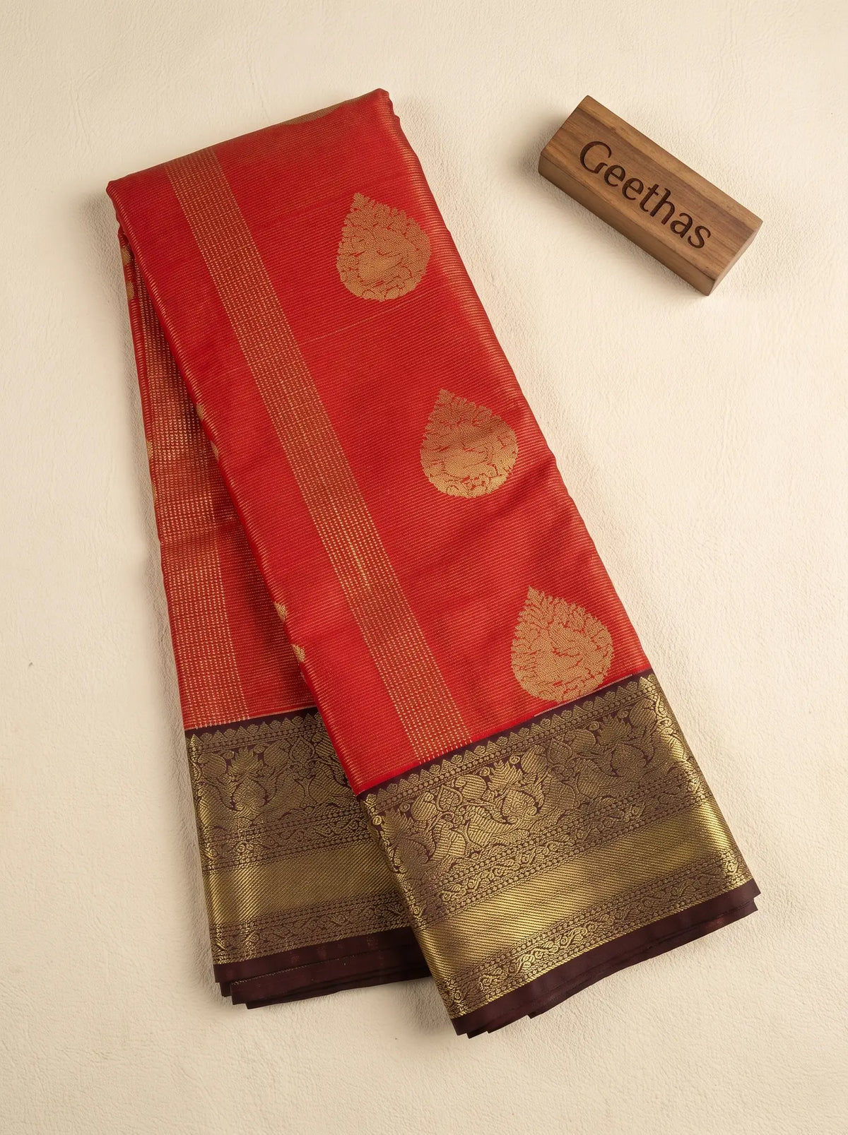 Folded burnt orange soft silk saree showing gold-toned paisley motifs and ornate zari border