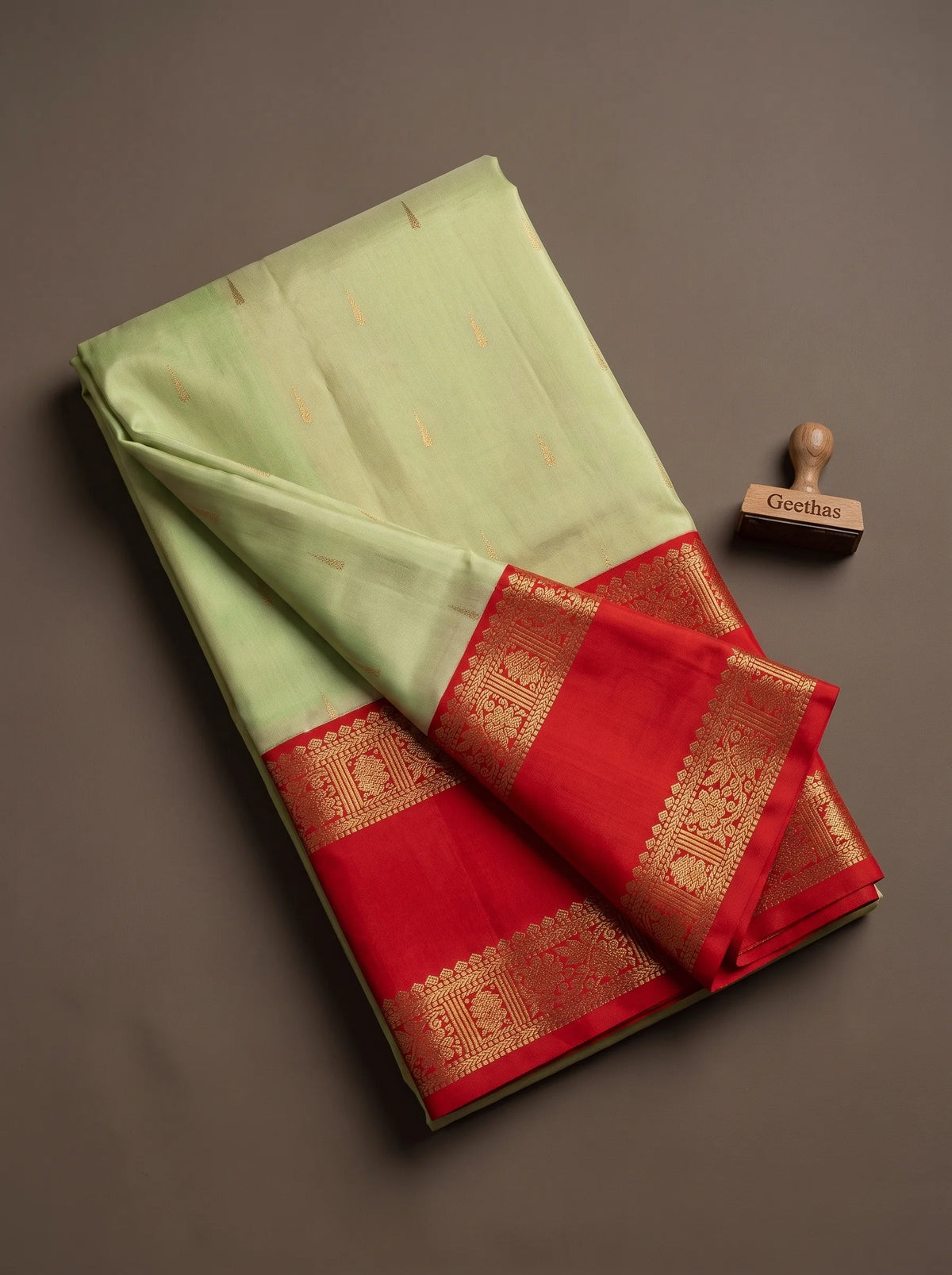 Pista green soft silk saree with gold-toned woven motifs and deep orange-red zari border, displayed folded