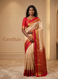 Model wearing an off-white soft silk saree with bright red and gold-toned zari border