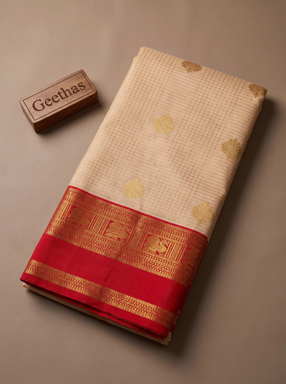 Folded off-white soft silk saree showing gold-toned woven motifs and bright red zari border