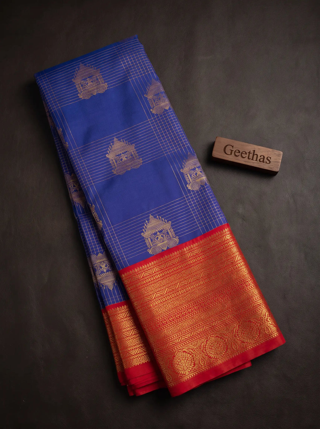 Folded royal blue saree showing gold-toned woven motifs, fine grid lines and a red zari border.