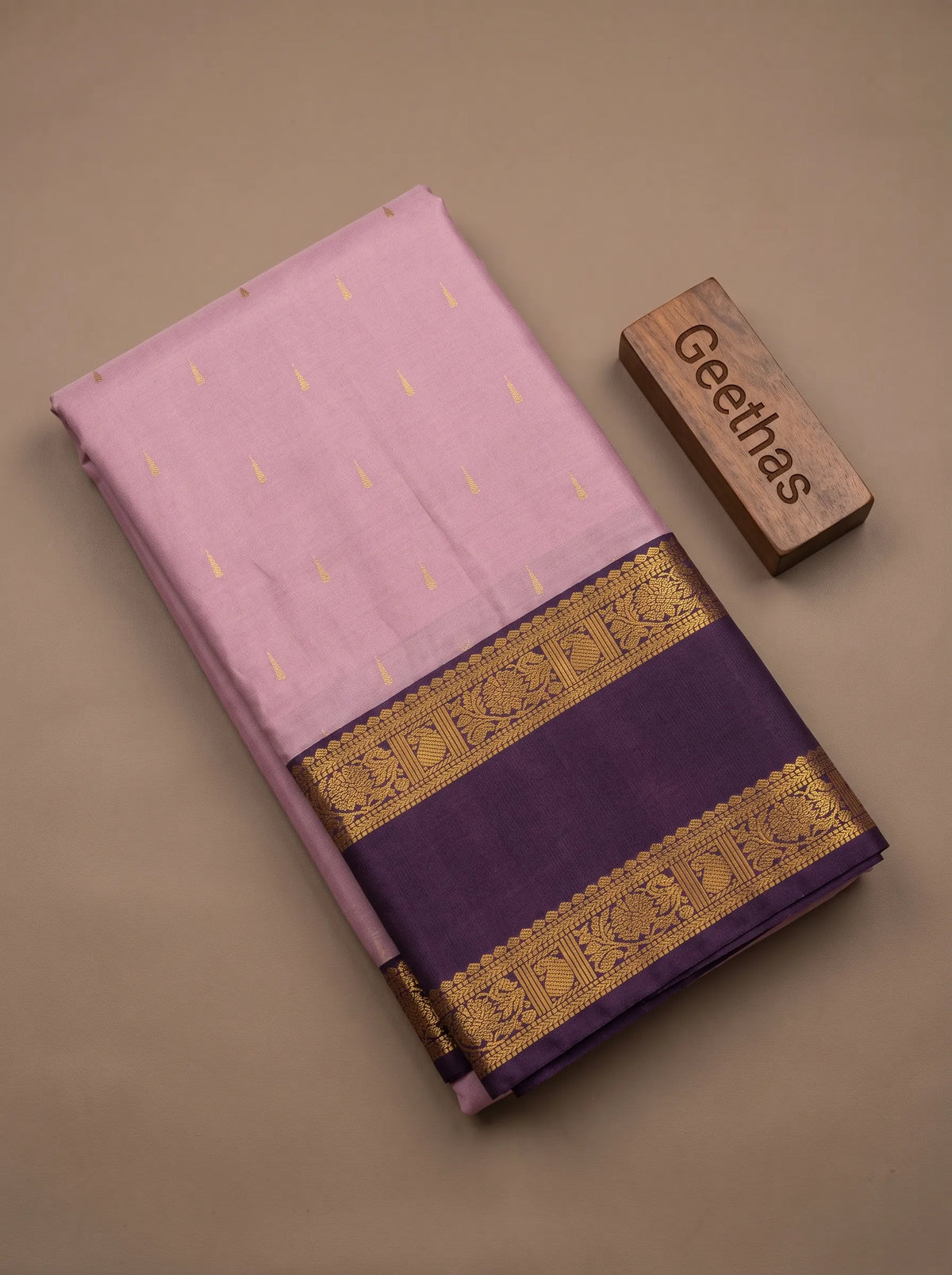 Folded onion pink soft silk saree with gold-toned woven motifs and a purple zari border
