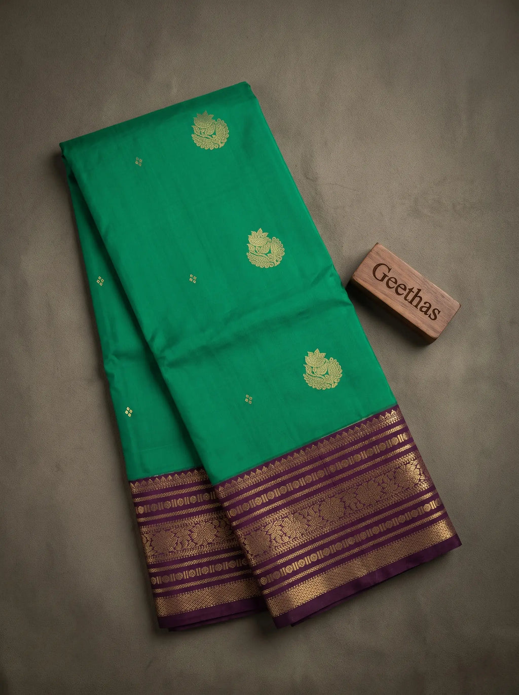 Emerald green soft silk saree with gold-toned woven motifs and a purple zari border displayed in a flat lay