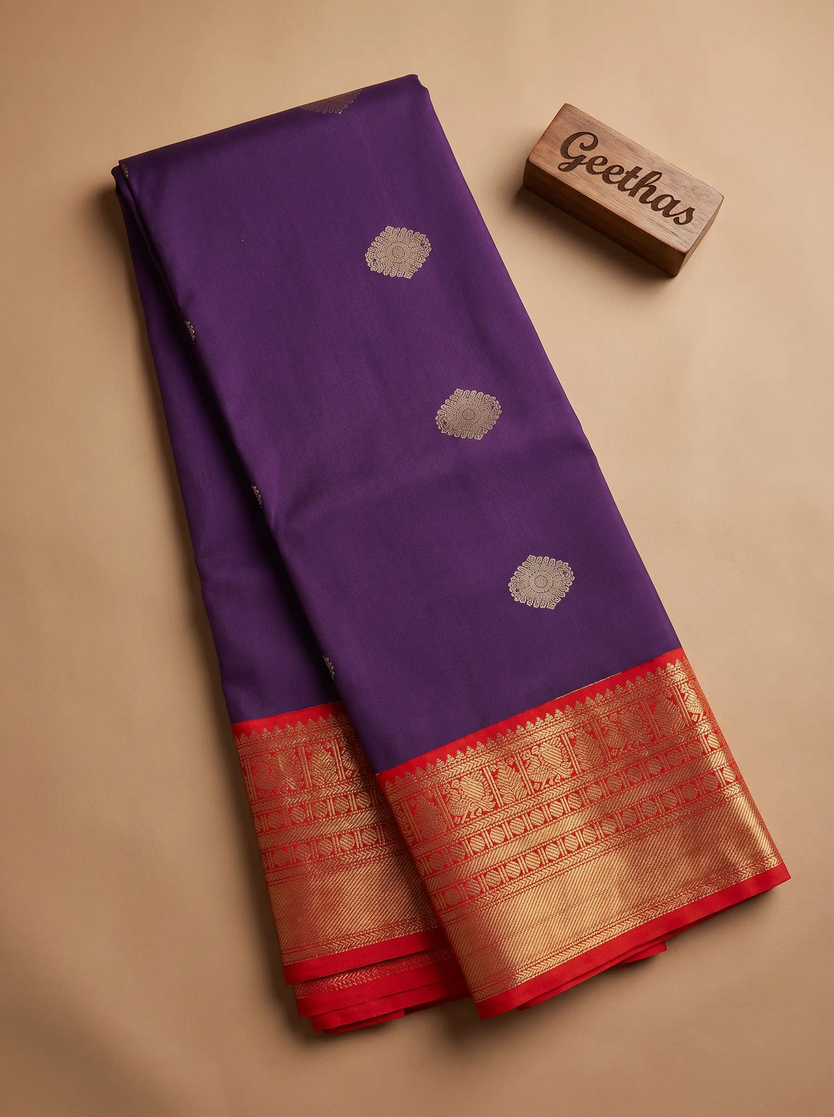 Folded deep blue soft silk saree showing gold-toned circular motifs and a red-edged zari border.