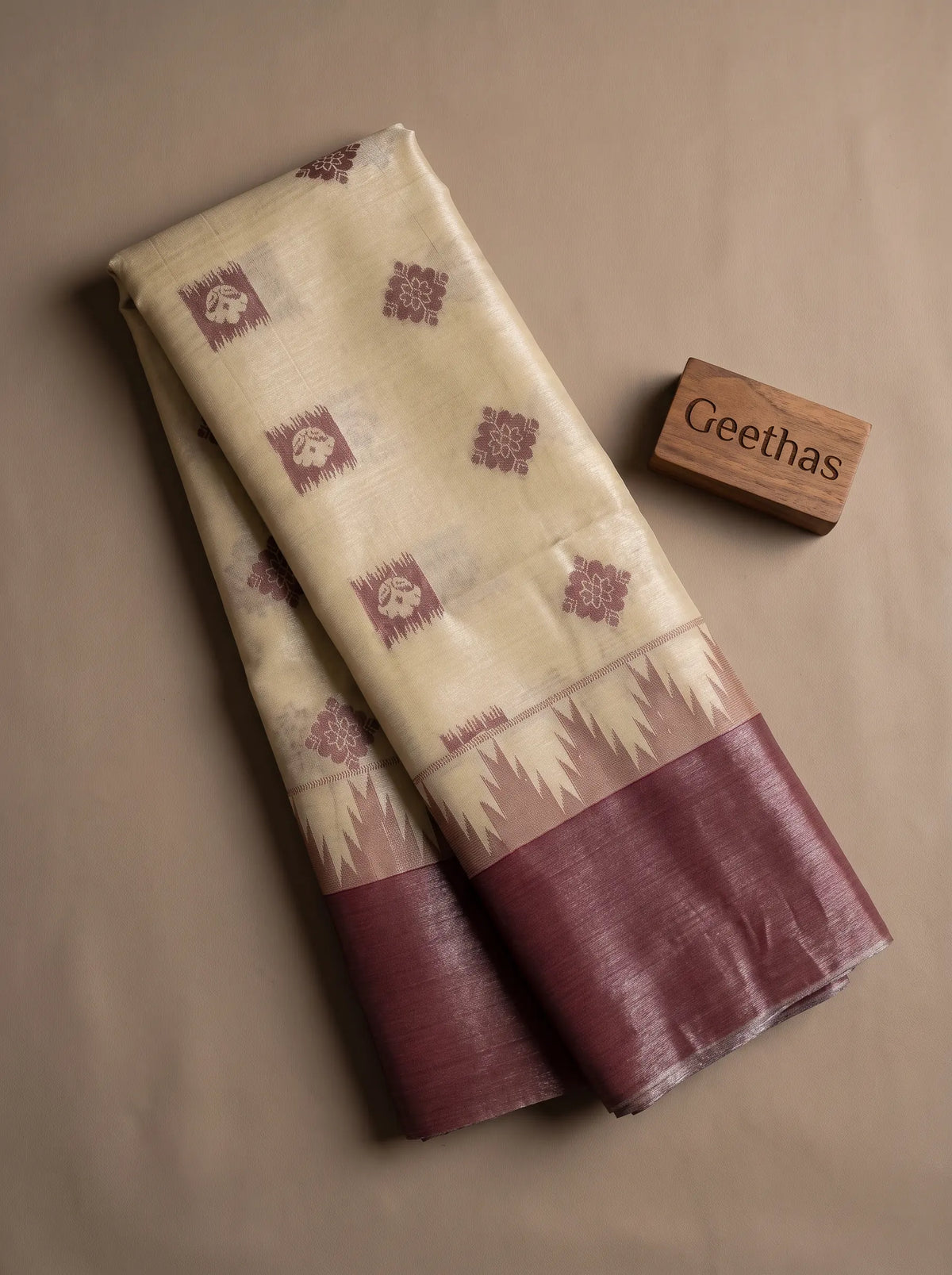 Folded beige tissue soft silk saree with burgundy woven motifs and contrasting border